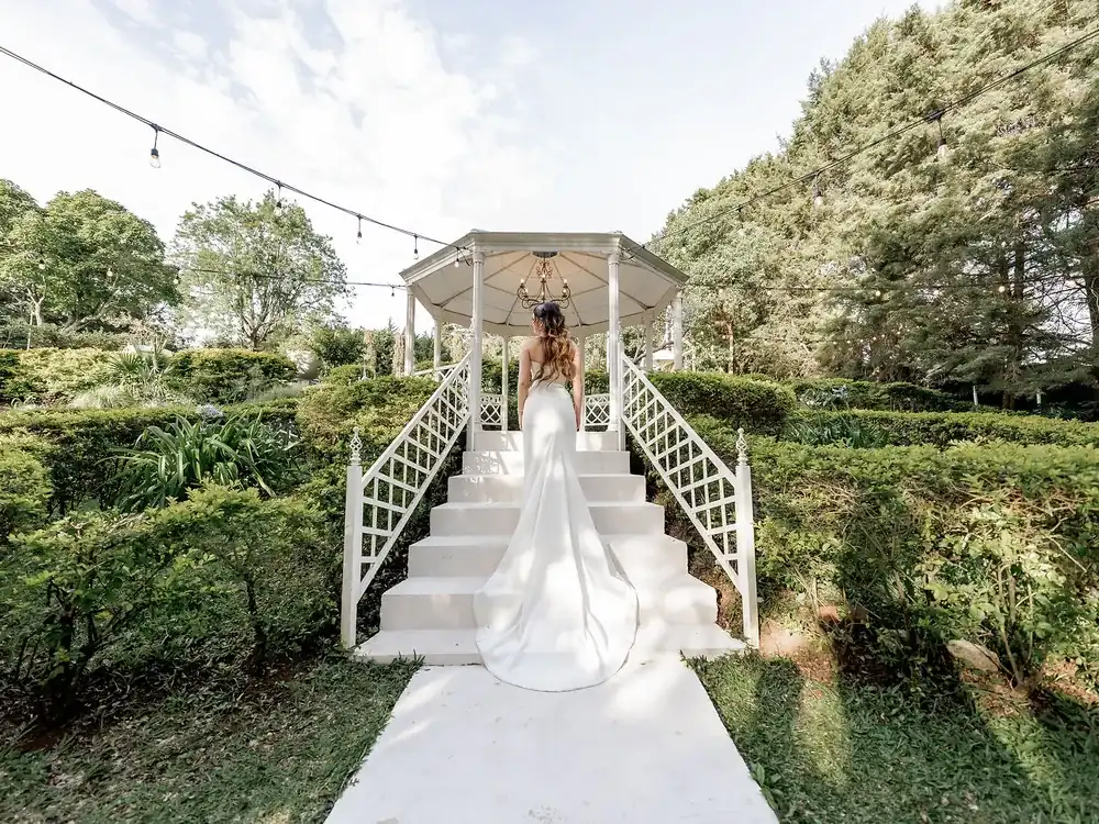 Novia bajando la escalinata blanca del Gazebo Jardín hacia la ceremonia