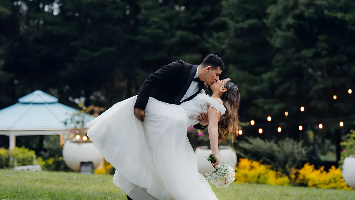 Novios besándose entre las urnas de piedra de los jardines de Laureal, con el gazebo iluminado al fondo