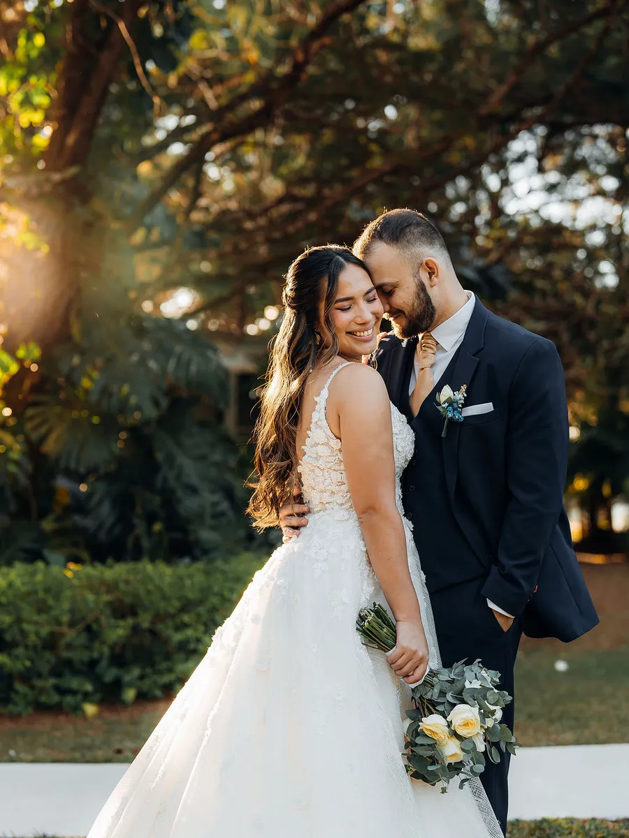 Novios abrazados en los jardines con el sol del atardecer entre los pinos
